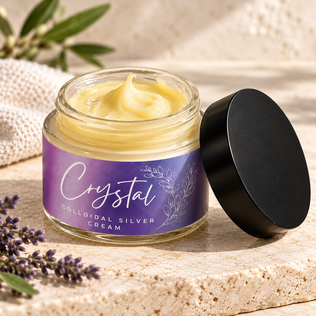Open jar of pale yellow cream with a purple Crystal Colloidal Silver Cream label and a black lid, with linen and leaves behind it.