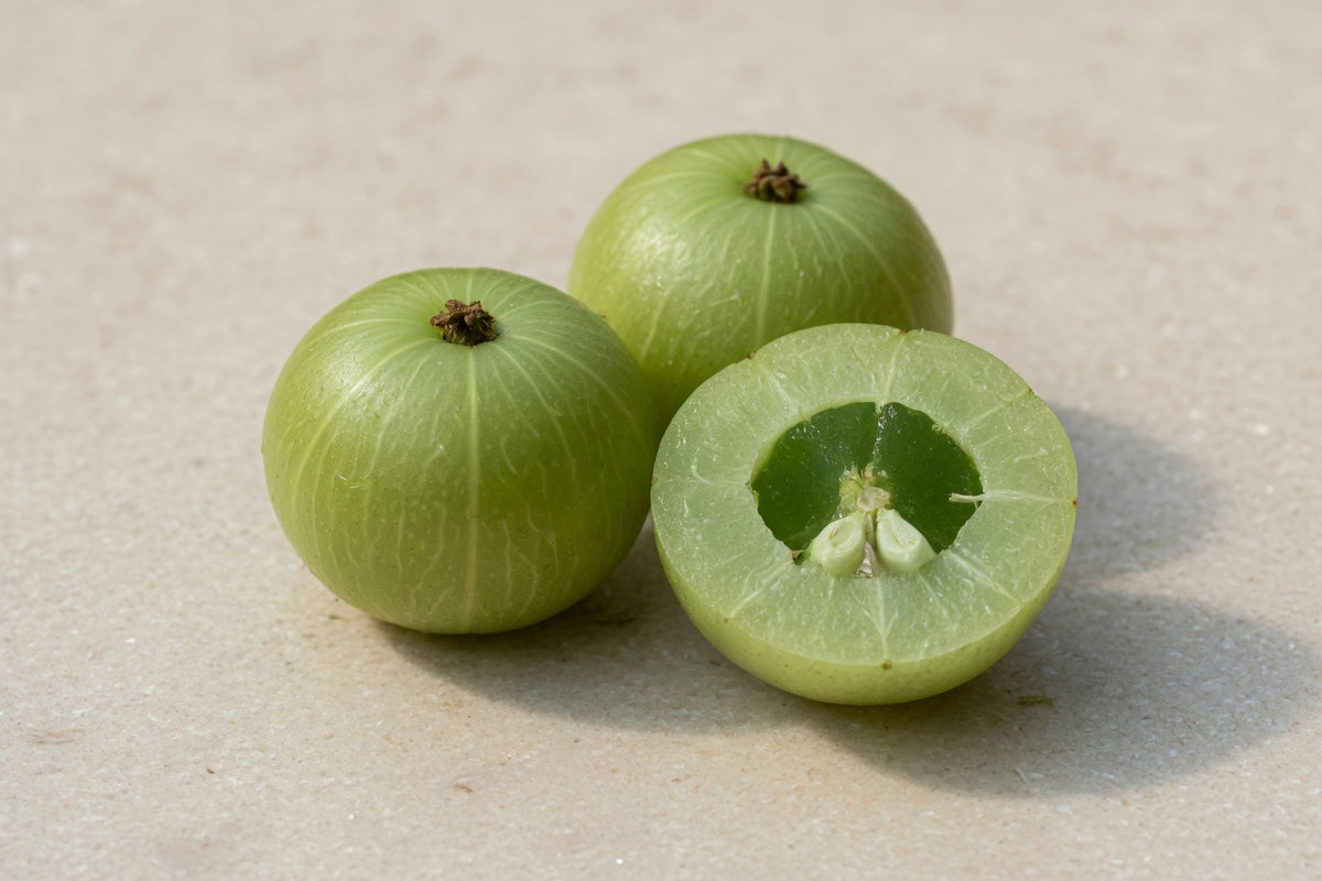 Pale green ribbed amla fruits, one cut open, on pale limestone.