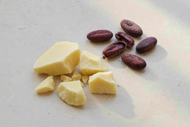 Pale cacao butter beside cacao beans on limestone.