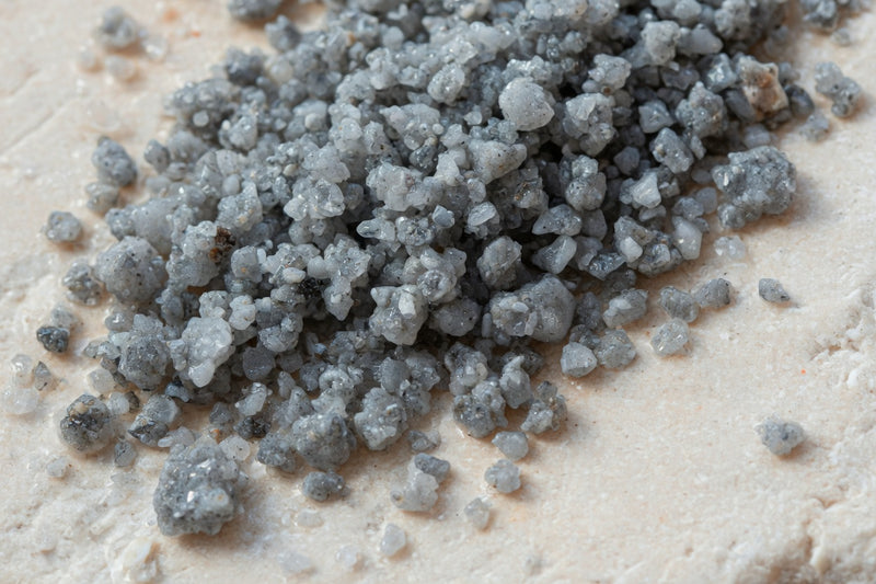 Moist grey coarse sea salt crystals on pale limestone.