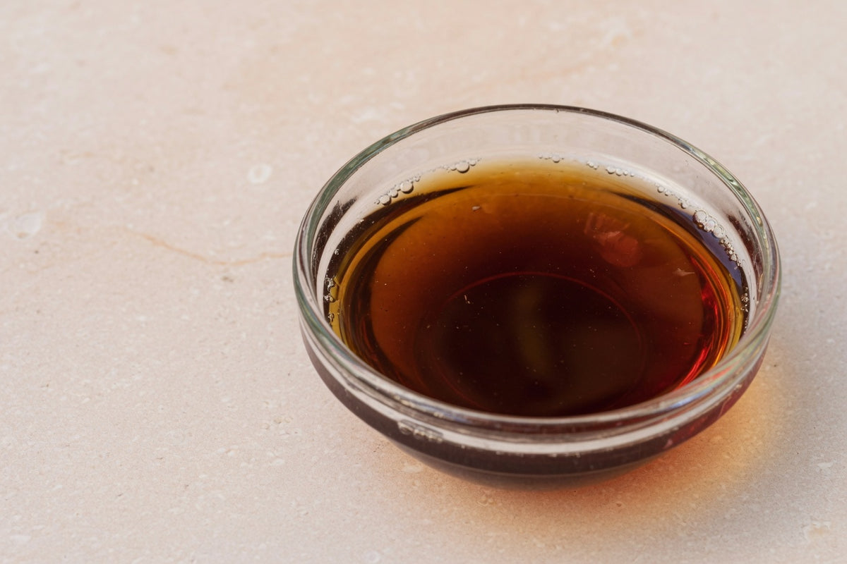 A glass dish of dark tea-brown liquid on pale limestone.