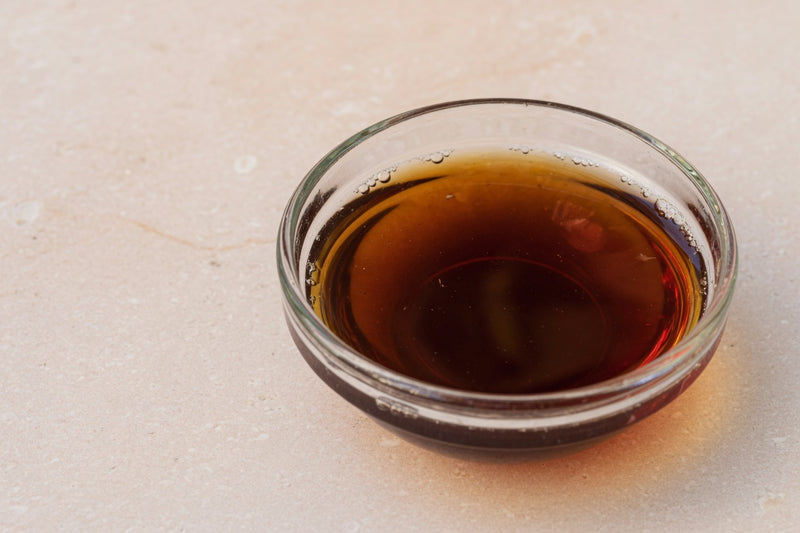 A glass dish of dark tea-brown liquid on pale limestone.