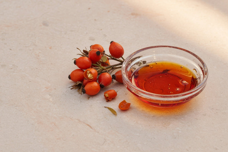 Orange-red rose hips beside a glass dish of reddish oil.