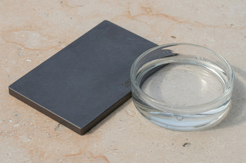 Matte dark titanium metal beside a glass dish of clear water.