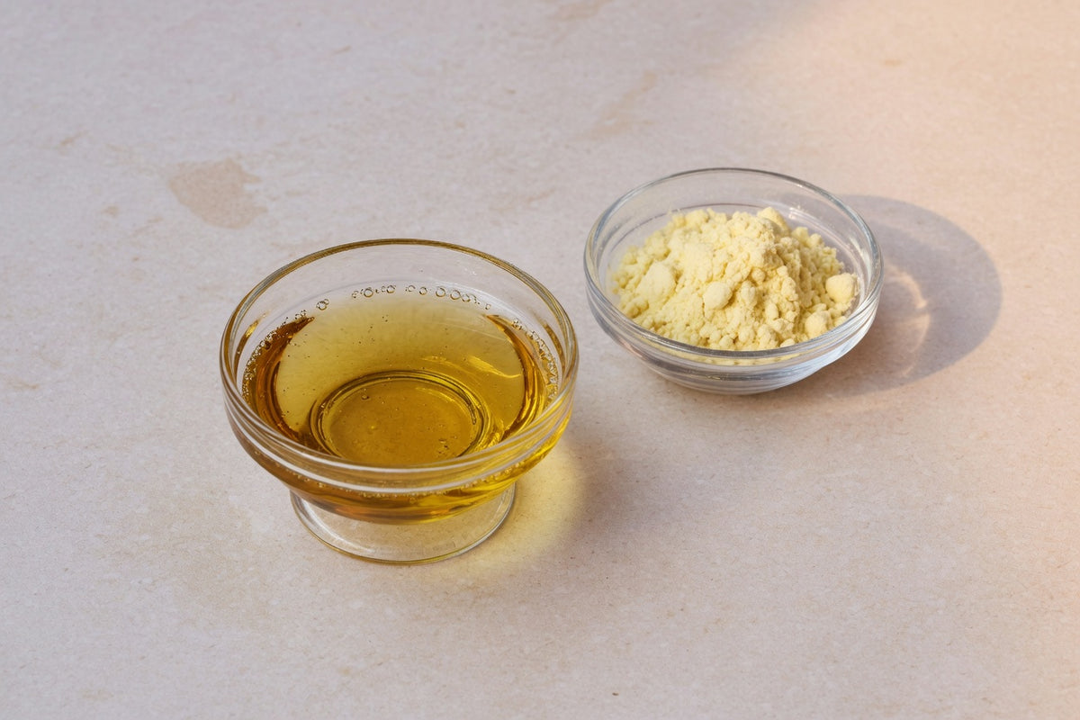 A glass dish of golden oil beside a dish of pale yellow powder, with no food.